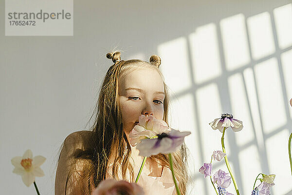 Mädchen riecht frische Blumen vor weißer Wand