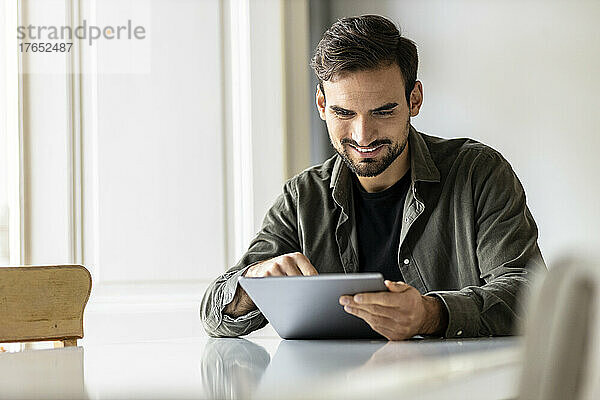 Lächelnder Mann  der zu Hause mit einem Tablet-PC am Tisch sitzt