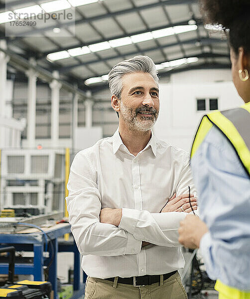 Geschäftsmann steht mit verschränkten Armen und diskutiert mit Ingenieur in der Fabrik