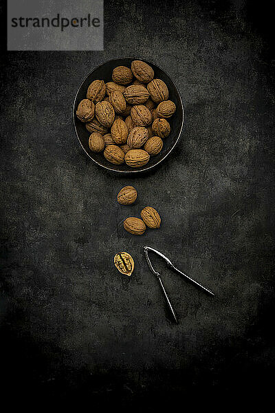 Studio shot of nutcracker and bowl of walnuts lying against black background