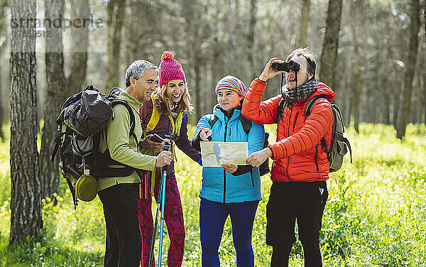 Mann schaut durch ein Fernglas und steht neben Freunden  die im Wald eine Karte teilen