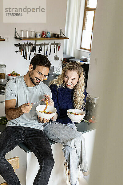 Smiling couple eating noodles in kitchen