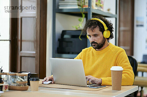 Geschäftsmann hört Musik über Kopfhörer mit Laptop am Schreibtisch im Büro