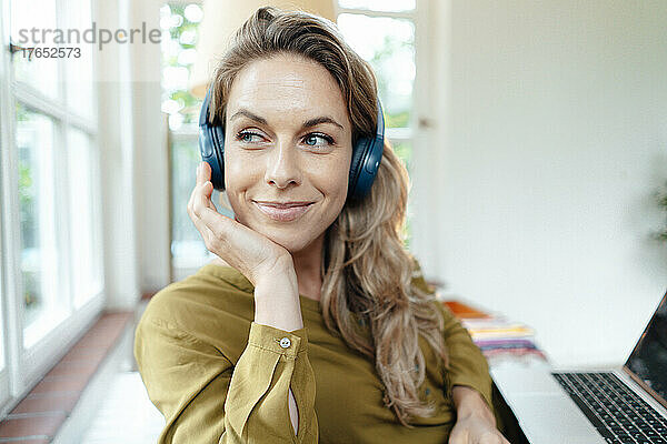 Lächelnde schöne Frau  die zu Hause Musik über kabellose Kopfhörer hört