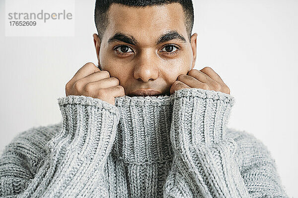 Mann bedeckt Gesicht mit grauem Wollpullover vor weißem Hintergrund