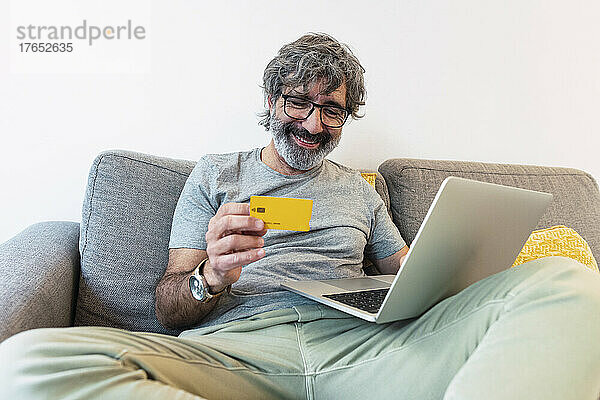 Glücklicher Mann nutzt Kreditkarte zum Bezahlen von Finanzrechnungen zu Hause