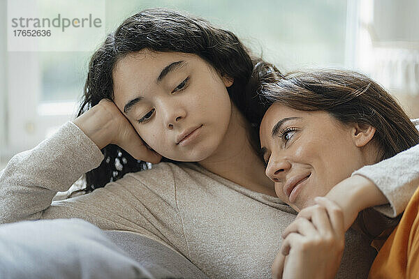 Teenage girl embracing smiling mother sitting on sofa at home