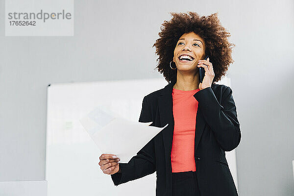 Glückliche Geschäftsfrau  die im Büro mit dem Mobiltelefon spricht