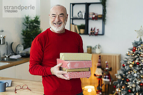 Glücklicher älterer Mann mit Geschenkboxen  der zu Hause am Tisch steht