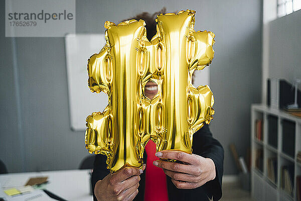 Geschäftsfrau hält goldenen Hashtag-Symbolballon vor Gesicht