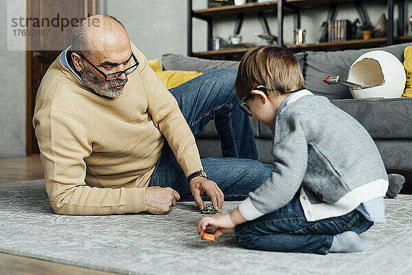 Älterer Mann und Enkel spielen mit Spielzeugauto im heimischen Wohnzimmer