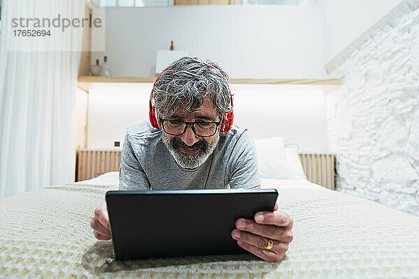 Mann mit Kopfhörern benutzt Tablet-PC im heimischen Bett