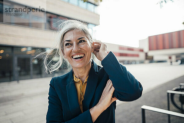 Fröhliche Geschäftsfrau mit der Hand im Haar im Büropark