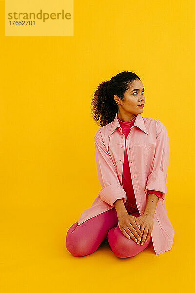 Junge Frau im rosa Hemd sitzt vor gelbem Hintergrund