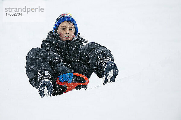 Junge mit Strickmütze rodelt im Winter im Schnee
