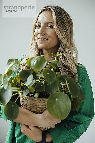 Smiling woman holding houseplant standing against white background