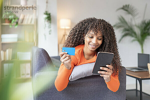 Lächelnde Frau mit Kreditkarte und Mobiltelefon zu Hause