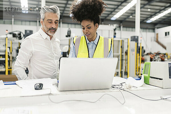 Ingenieur diskutiert über Laptop mit Geschäftsmann am Schreibtisch in der Fabrik