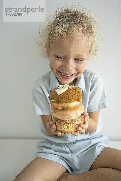 Smiling girl holding stack of doughnuts sitting on table