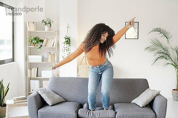 Lächelnde junge Frau tanzt zu Hause auf dem Sofa im Wohnzimmer