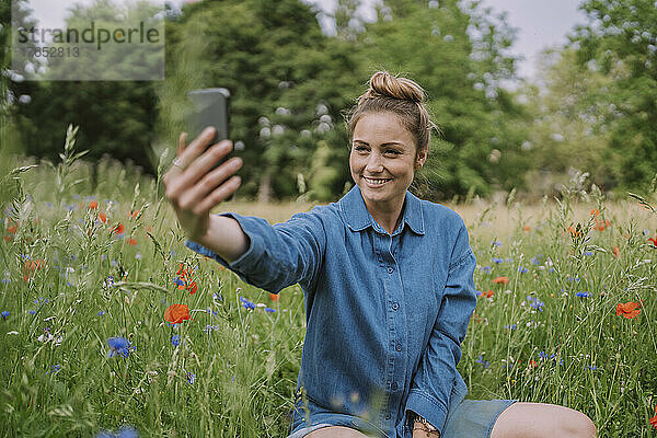 Lächelnde Frau macht Selfie mit Smartphone auf der Wiese