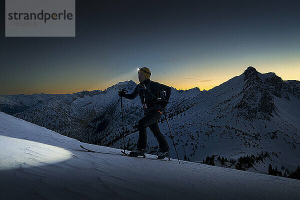 Mann mit Stirnlampe läuft auf schneebedecktem Berg