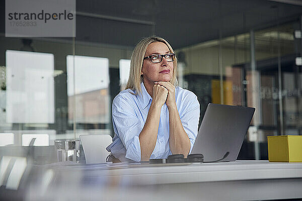 Geschäftsfrau mit Brille und Laptop am Schreibtisch im Büro