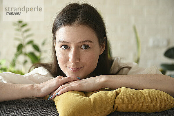 Smiling woman with yellow pillow sitting at home