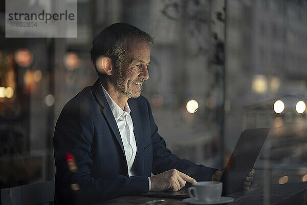 Lächelnder Freiberufler  der nachts im Café am Laptop arbeitet