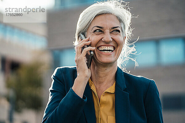 Fröhliche Geschäftsfrau mit grauem Haar  die auf dem Smartphone spricht