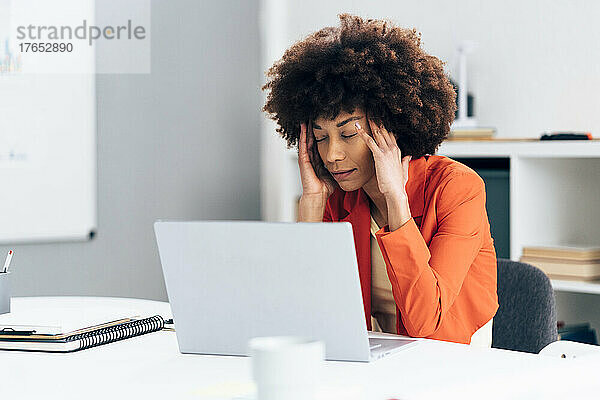 Geschäftsfrau mit Kopf in den Händen sitzt mit Laptop am Schreibtisch im Büro