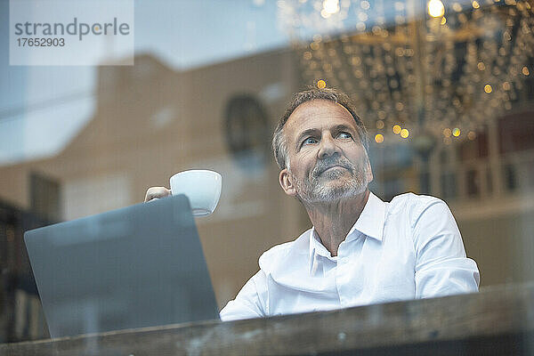 Geschäftsmann mit Kaffeetasse und Laptop sitzt im Café