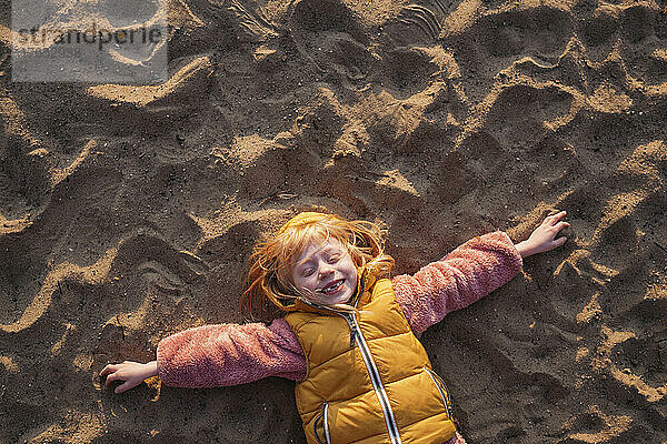 Playful girl with blond hair lying on sand