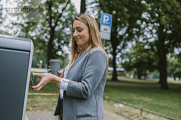 Frau bezahlt Rechnung per Mobiltelefon an Elektroladestation