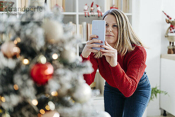 Frau fotografiert zu Hause den Weihnachtsbaum per Handy