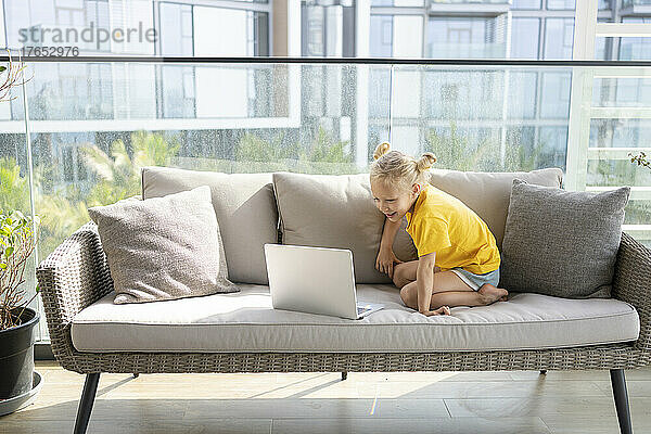 Smiling girl looking at laptop sitting on sofa at home