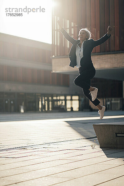 Glückliche Geschäftsfrau springt an einem sonnigen Tag im Büropark