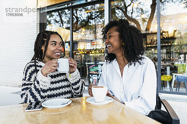 Glückliche Geschäftsfrauen mit Kaffeetassen sitzen im Straßencafé