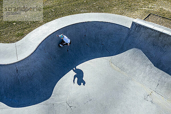 Junger Skateboarder übt an sonnigem Tag auf dem Pumptrack