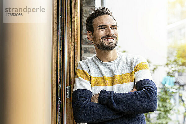 Smiling man with arms crossed leaning on door frame