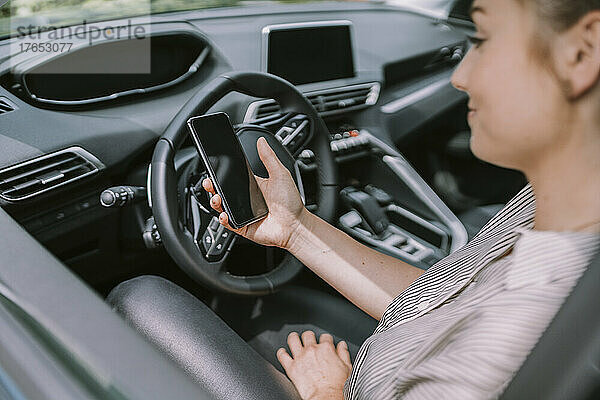 Frau mit Smartphone sitzt auf dem Fahrersitz im Auto