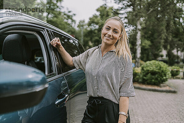 Lächelnde Frau steht mit dem Auto auf dem Parkplatz