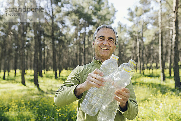 Glücklicher reifer Mann mit Plastikflaschen  der im Wald steht