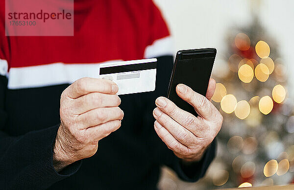Hand eines älteren Mannes  der zu Hause Kreditkarte und Mobiltelefon hält