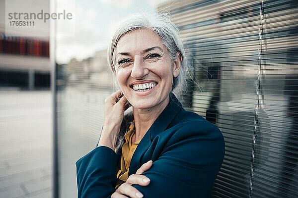 Cheerful businesswoman with gray hair by glass wall
