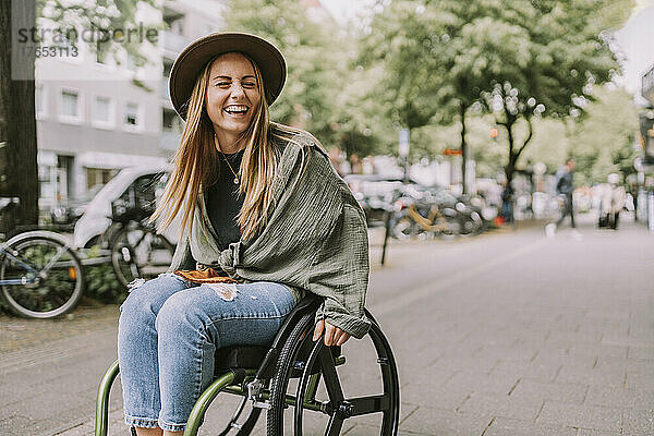 Fröhliche junge Frau sitzt im Rollstuhl am Bürgersteig