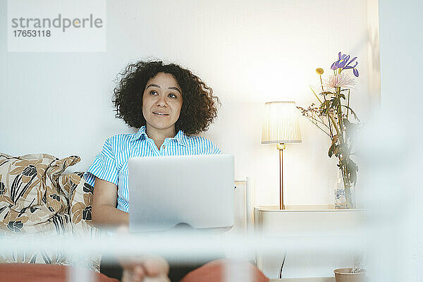 Frau mit Laptop sitzt zu Hause im Bett