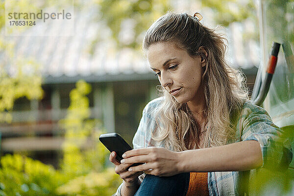 Blonde Frau schreibt Textnachrichten per Smartphone im Hinterhof