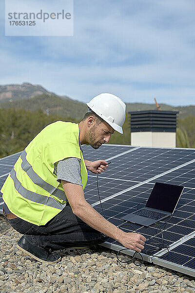 Ingenieur mit Laptop-Stromversorgungskabel vor Sonnenkollektoren an einem sonnigen Tag