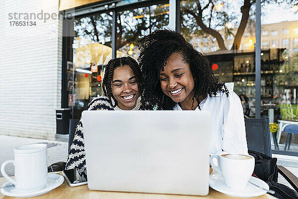 Glückliche Kollegen mit Laptop sitzen im Straßencafé
